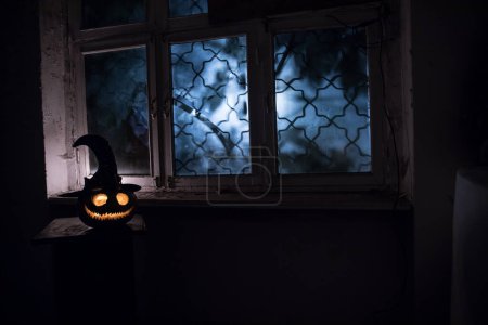 Photo for Scary Halloween pumpkin in the mystical house window at night or halloween pumpkin and horror silhouette in window. Selective focus - Royalty Free Image