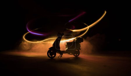 Téléchargez les photos : Silhouette de scooter miniature debout sur fond sombre avec de la lumière. Concentration sélective - en image libre de droit
