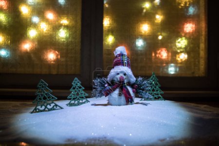 Photo for Christmas and New year concept.Fir tree standing on snow with beautiful holiday decorated background and traditional holiday attributes. Cozy window with colorful lights on background. Selective focus - Royalty Free Image