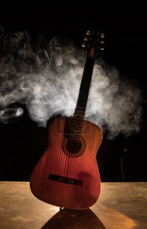 Musikkonzept. Akustikgitarre isoliert auf dunklem Hintergrund unter Lichtkegel mit Rauch und Kopierraum. Gitarrensaiten, hautnah. Selektiver Fokus.