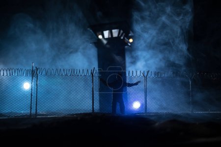 Photo for Criminal justice imprisonment concept or prison break concept. Silhoette of prisoner standing near of prison fence with watchtower at night. Creative art decoration. Selective focus - Royalty Free Image