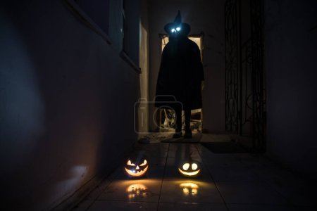 Téléchargez les photos : Concept d'Halloween. Silhouette effrayante dans le couloir sombre avec tête de citrouille. Lumière tonique avec brouillard sur le fond. Concentration sélective. Long coup d'obturateur - en image libre de droit