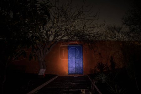 Foto de Luna llena sobre pueblo tranquilo por la noche. Pared naranja con puerta metálica azul por la noche. Atmósfera de horror embrujada. Disparo de larga exposición - Imagen libre de derechos