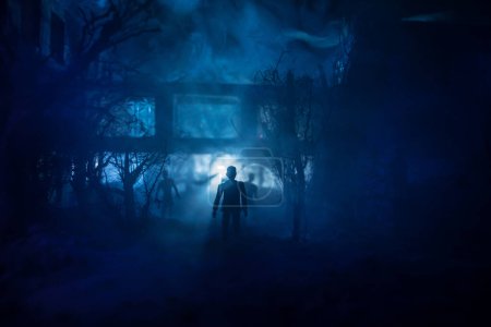 Téléchargez les photos : Silhouette de personne debout dans la forêt sombre avec de la lumière. Horreur concept d'Halloween. étrange silhouette au bâtiment abandonné - en image libre de droit
