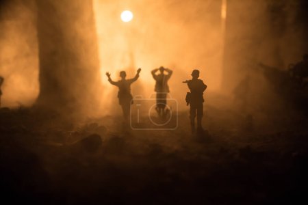 Foto de Siluetas militares peleando escena en el fondo del cielo niebla de guerra. Un soldado alemán levantó las armas para rendirse. Soldados de juguete de plástico con armas tomando prisionero al soldado enemigo. Enfoque selectivo - Imagen libre de derechos