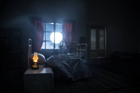Foto de Concepto de Halloween de horror. Una casa de muñecas realista dormitorio con muebles y ventana por la noche. Hombre asustado en la cama con luna llena afuera. Decoración creativa. Enfoque selectivo - Imagen libre de derechos