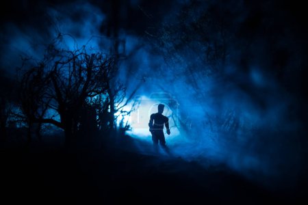 Foto de Silueta de persona de pie en el bosque oscuro con luz. Concepto de Halloween de horror. extraña silueta en un oscuro pueblo espeluznante - Imagen libre de derechos