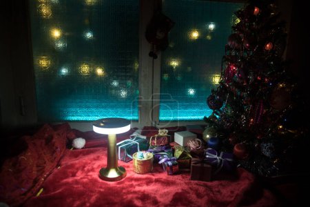 Foto de Navidad y Año Nuevo concept.Fir árbol de pie sobre alfombra roja con atributos tradicionales de vacaciones. Acogedora ventana con luces de colores en el fondo. Enfoque selectivo - Imagen libre de derechos