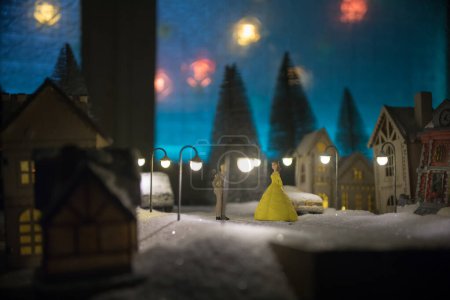 Téléchargez les photos : Petites maisons décoratives mignonnes dans la neige la nuit en hiver, Noël et Nouvel An maison miniature dans la neige la nuit avec sapin. Concept de vacances. Concentration sélective - en image libre de droit