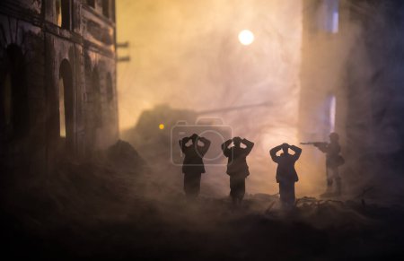 Téléchargez les photos : Silhouettes militaires combattant scène sur fond de brouillard de guerre ciel. Un soldat allemand leva les armes pour se rendre. Soldats jouets en plastique avec des fusils faisant prisonnier le soldat ennemi. Concentration sélective - en image libre de droit
