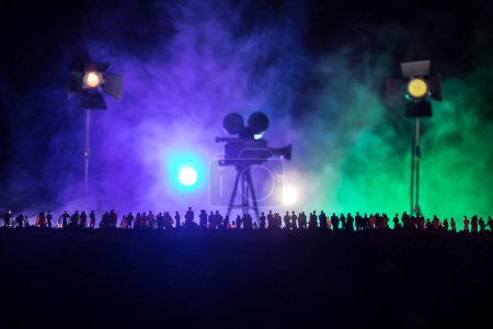 Filmkonzept: Menschenmenge gegen riesige Filmkamera im Dunkeln. Silhouette einer Vintage-Kamera auf Stativ. Selektiver Fokus