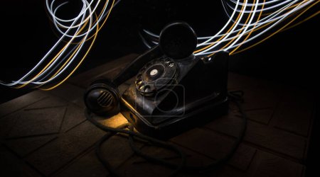 Téléchargez les photos : Vieux téléphone noir sur vieille planche de bois avec fond sombre art avec brouillard et lumière tonique. espace vide. Concentration sélective - en image libre de droit