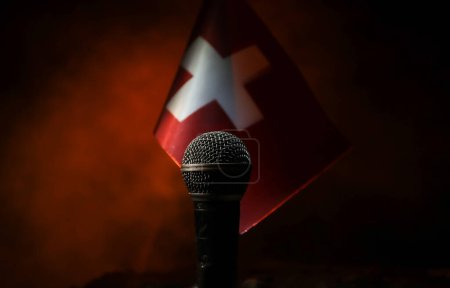 Microphone on a background of a blurry flag of Switzerland close-up. dark table decoration. Selective focus