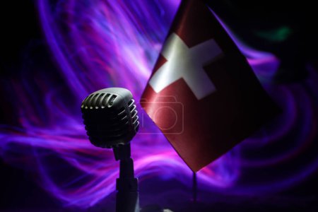 Micrófono en un fondo de una bandera borrosa de Suiza primer plano. decoración de mesa oscura. Enfoque selectivo