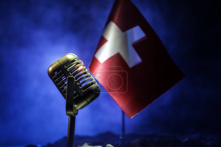 Mikrofon auf dem Hintergrund einer verschwommenen Flagge der Schweiz in Großaufnahme. dunkle Tischdekoration. Selektiver Fokus