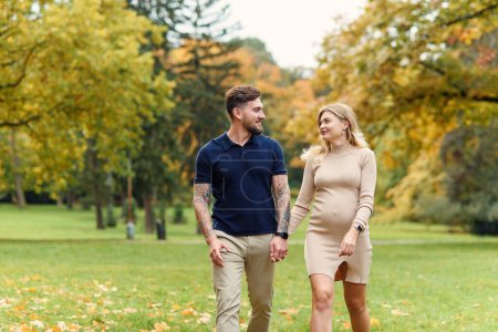 Foto de Elegante joven embarazada y su marido guapo están caminando en el parque de otoño. - Imagen libre de derechos