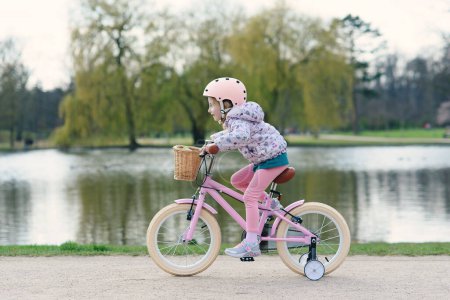 Photo for Little girl riding bike in safe helmet at sunny spring park near big lake. Preschooler learning to balance on bicycle in safe helmet. - Royalty Free Image