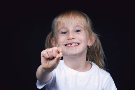 Photo for Six year old blondy smiling happy girl holding a fallen baby tooth. - Royalty Free Image