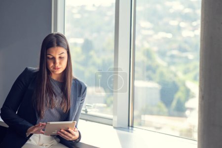 Photo for Young attractive female manager working on digital tablet while standing in modern office. - Royalty Free Image