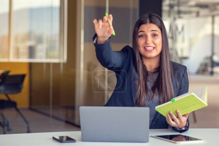 Photo for Photo of pretty young girl sit desktop pc hold pen write notepad wearing shirt in home office indoors - Royalty Free Image