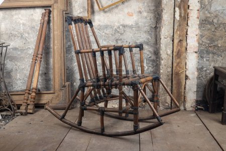 Téléchargez les photos : Une vieille chaise berçante en bambou se trouve dans une pièce sale, sur le vieil étage à côté d'autres choses vintage - en image libre de droit