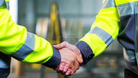 Photo for Close up of Caucasian men shaking hands at factory as sign of agreement and good work together. Inside. Males constructors or builders shake hands. Gesture of agreeing of two workmen at manufactory. - Royalty Free Image