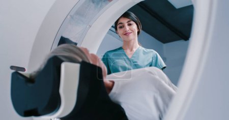 Imágenes de resonancia magnética terminadas en hembra, el paciente se está moviendo fuera de la cápsula del escáner de resonancia magnética. La doctora le pregunta al paciente sobre el bienestar después de examinarlo. El doctor sonríe y habla con la mujer..