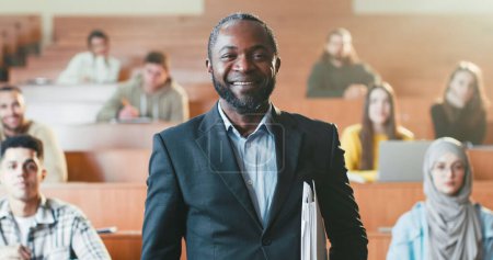 Photo for Portrait shot of cheerful African American male professor crossing hands in front of camera and laughing. University. Students on background. Happy man teacher of high school with folder of papers. - Royalty Free Image