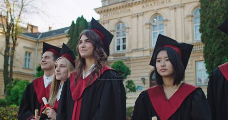 Téléchargez les photos : Multiethnique jeunes filles heureuses diplômés en casquettes et robes rire et s'amuser à la cérémonie de remise des diplômes à l'université
. - en image libre de droit