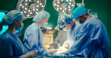 Multiracial team of professional medical surgeons performs surgical operation in modern hospital. Male and female doctors are working to save patient. Concept of medicine and treatment.