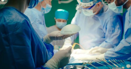 Ein multikulturelles Team professioneller plastischer Chirurgen führt plastische Chirurgie in einer modernen Privatklinik durch. Chirurgen und Anästhesisten arbeiten im Operationssaal. Konzept der Medizin und Behandlung.