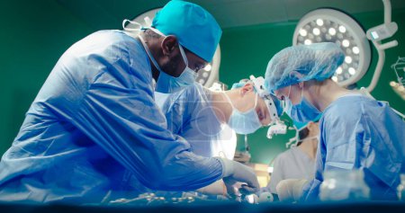 Multiracial team of professional medical surgeons performs surgical operation in modern hospital. Male and female doctors are working to save patient. Concept of medicine and treatment.
