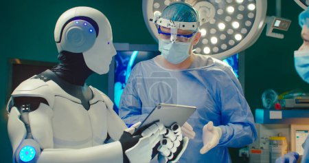 Foto de Primer plano retrato Robot celebración tableta digital ayuda al médico a realizar la operación quirúrgica en el hospital moderno. Trabajo en equipo de cirujanos médicos profesionales en quirófano. - Imagen libre de derechos