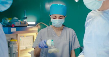 Photo for Medical workers in special clothes. Doctors at background of medical equipment in surgery room. African American assistant holds tweezers with cotton wool. Intern holds patients breathing tube. - Royalty Free Image