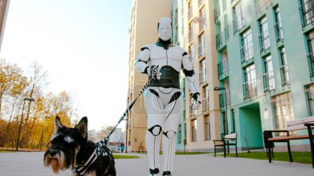 Pretty scottish terrier dog walking on long leash with housemaid white android robot along urban alley. Smart human assistant cyborg outdoors. Robotics industry.