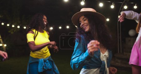Close up of beautiful mixed-race girls dancing in garden at party. Caucasian and African American cheerful females having fun. Happy handsome guy moving to music. Gathering together on summer evening