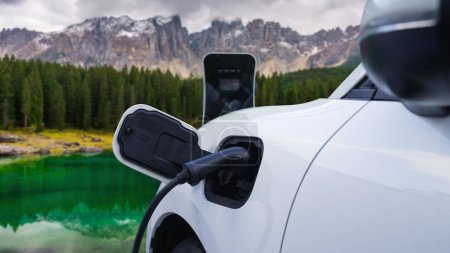 Nachhaltiger Autoverkehr durch Elektrogeneratorantrieb, Aufladen der Batterie an der Ladestation mit Gebirgshintergrund für progressives Reisekonzept. Elektroauto in der Natur als Symbol für saubere Umwelt.