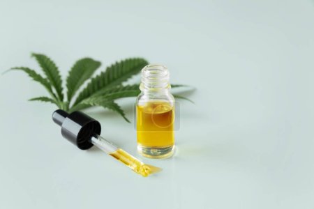Cannabis sativa hemp leaf with container of CBD oil with dropper lid on white background. Legalized marihuana concept.