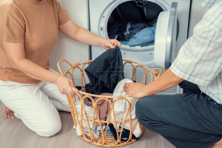 Photo for Senior couple working together to complete their household chores at the washing machine in a happy and contented manner. Husband and wife doing the usual tasks in the house. - Royalty Free Image