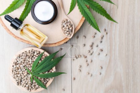 Cannabis and cosmetic concept features with set of CBD oil bottles, cream jar, and wooden bowl of hemp seeds. Legalized cannabis for skincare products.
