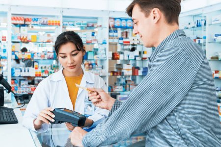 Photo for Payment by credit card with payment terminal in qualified drugstore. Modern financial payment of electric money. Caucasian customer purchase medication in pharmacy with prescription from pharmacist. - Royalty Free Image