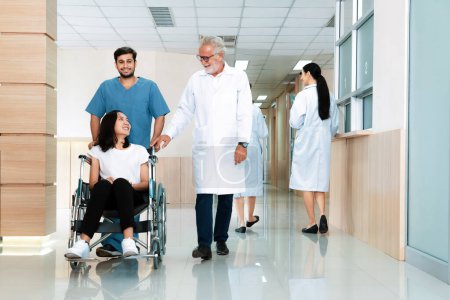 Téléchargez les photos : Médecin et infirmier transportent une patiente en fauteuil roulant le long d'un couloir stérile de l'hôpital. Soins de santé et soins infirmiers pour les patients handicapés dans le concept hospitalier. - en image libre de droit