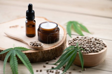 Photo for Cannabis and cosmetic concept features with set of CBD oil bottles, cream jar, and wooden bowl of hemp seeds. Legalized cannabis for skincare products. - Royalty Free Image