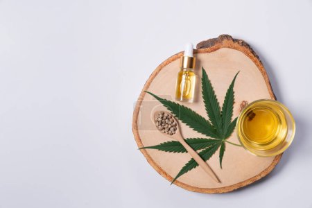 Set legalisiertes Marihuana enthält grünes Hanfblatt, CBD-Öl in einer Flasche mit Tropfdeckel und Glasschale und Hanfsamen auf einem Holzteller.