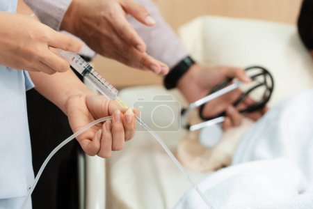 Photo for Doctor and nurse inject medicine, dosage into IV tube providing medical treatment to patient in sterile room at hospital. Fragile patient receive medical care on sick bed in recovery room. - Royalty Free Image