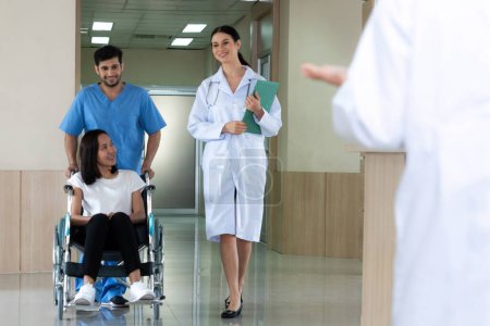 Téléchargez les photos : Médecin et infirmier transportent une patiente en fauteuil roulant le long d'un couloir stérile de l'hôpital. Soins de santé et soins infirmiers pour les patients handicapés dans le concept hospitalier. - en image libre de droit