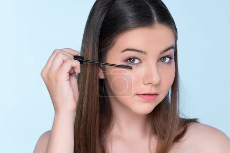 Foto de Closeup portrait of young charming applying makeup eyeshadow on her face with brush, mascara with flawless smooth skin for beauty concept. - Imagen libre de derechos