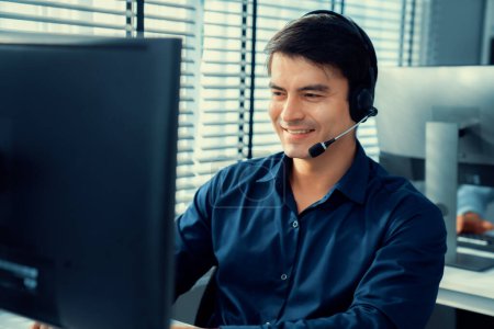 Photo for Young competent asian male call center agent working at his computer while simultaneously speaking with customers. Concept of an operator, customer service agent working in the office with headset. - Royalty Free Image