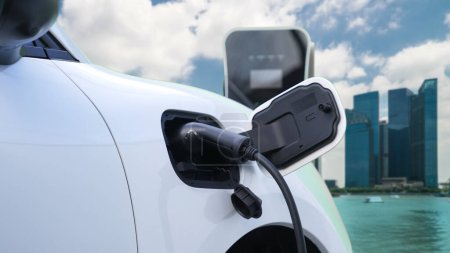 Vehículo eléctrico, coche EV recarga energía de la batería en la estación de carga en la autopista en el área urbana rodeada de rascacielos altos. Concepto ecológico de energía limpia progresiva.