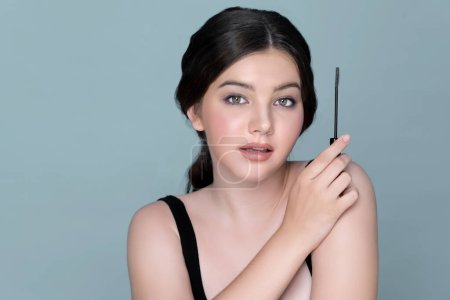 Foto de Closeup portrait of young charming applying makeup eyeshadow on her face with brush, mascara with flawless smooth skin for beauty concept. Luxury cosmetic makeup. - Imagen libre de derechos